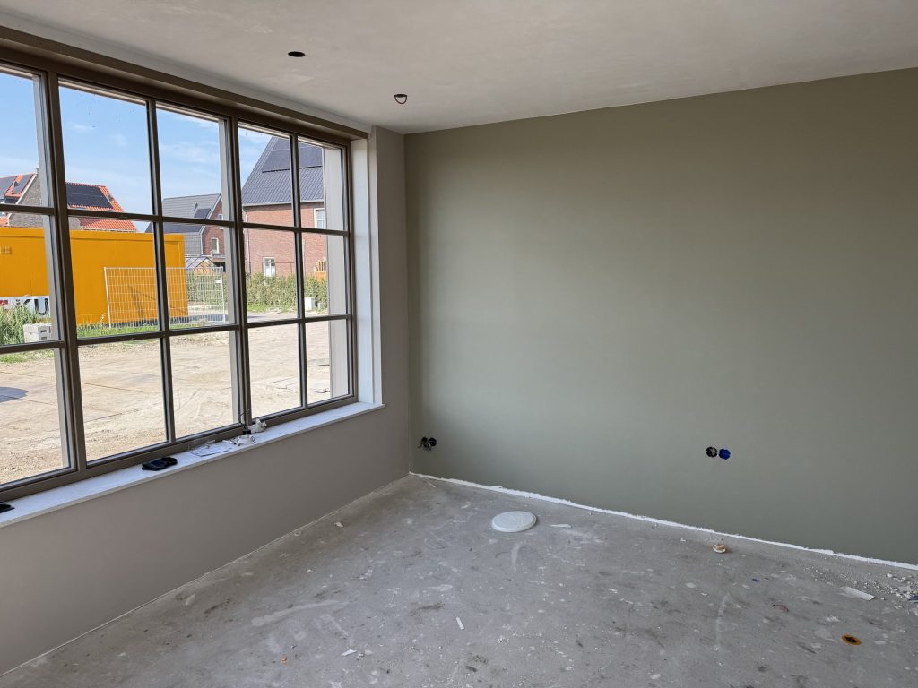 Nieuwbouwkamer met een egaal afgewerkte grijsgroene wand en een groot raam met roedeverdeling