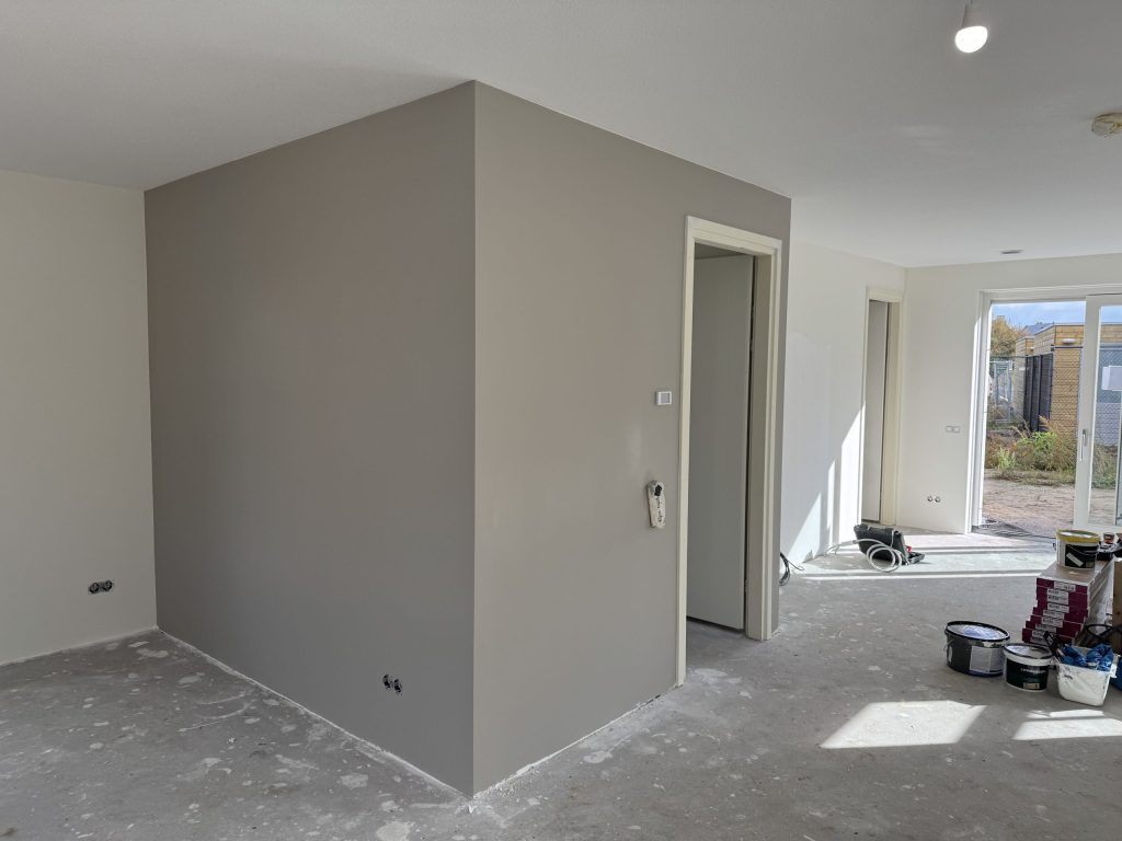 Open nieuwbouwruimte met een pas gesausde grijze wand en verfemmers bij de tuindeuren