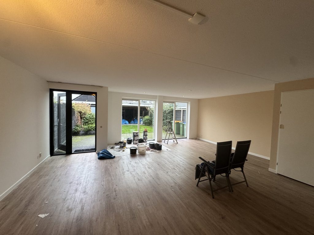 Ruime woonkamer met lichte gesausde wanden, houten vloer en tuindeuren tijdens de afwerking