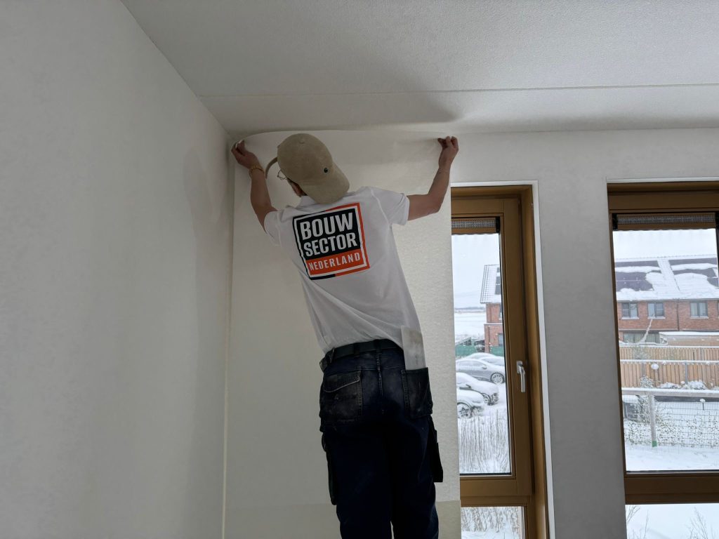 Behanger zet een baan vlies bovenaan de wand, tegen het plafond
