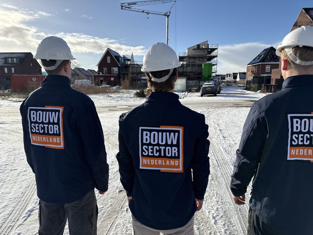 Drie vakmensen van Bouwsector Nederland met helm kijken naar woningen in aanbouw